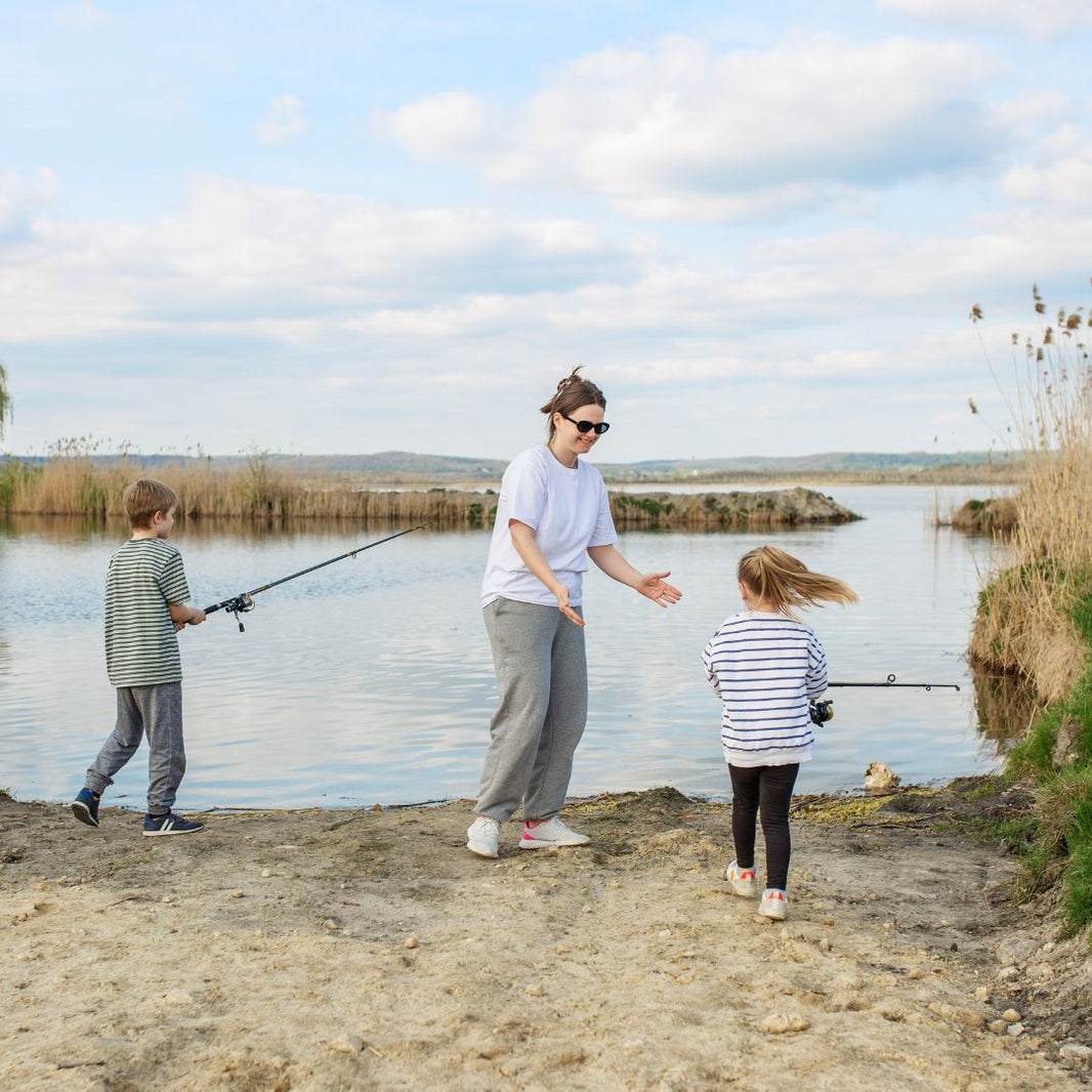 Woman and two children fishing by a lake on a sunny day