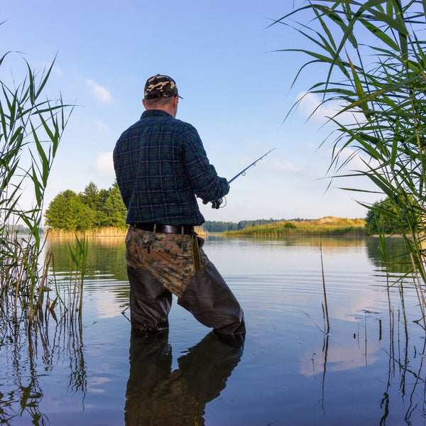 Man fishing in a calm lake surrounded by reeds on a clear day