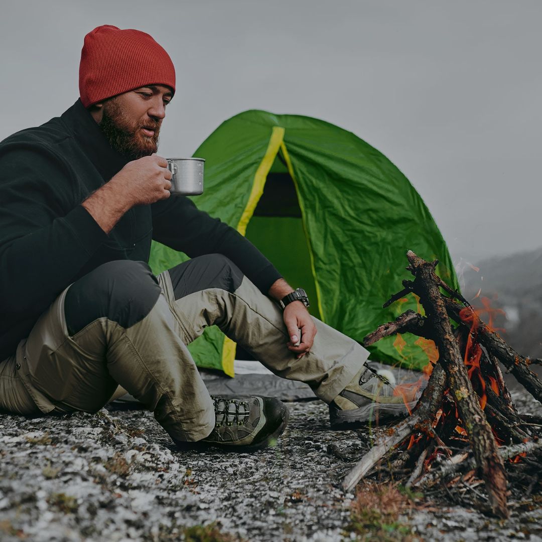 Man sitting by a campfire with a green tent in the background