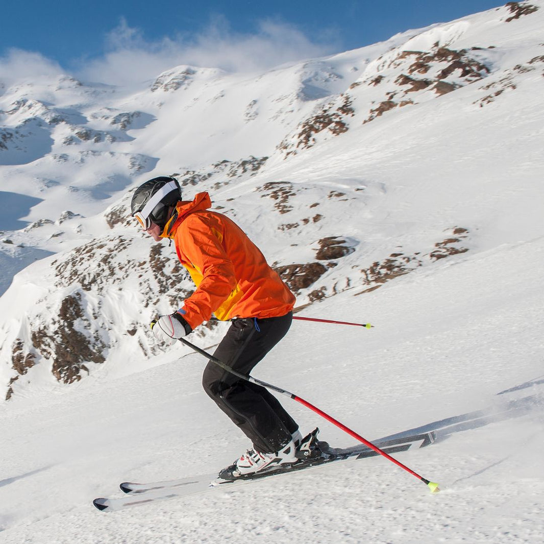 Person skiing down a snowy mountain with a bright orange jacket and helmet.